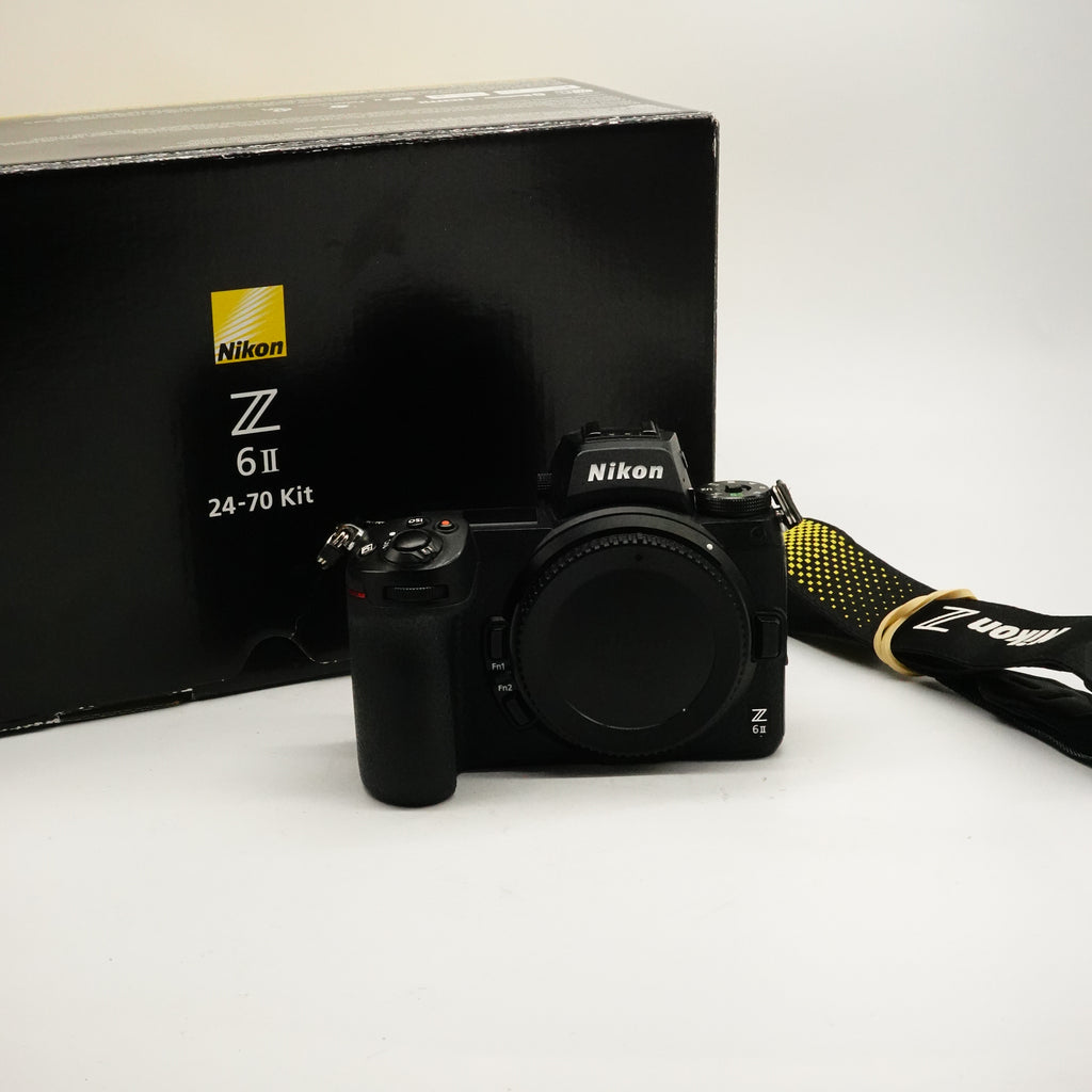 A Nikon Z 6 II mirrorless camera with a black grip and strap, positioned in front of its original black packaging box on a white studio background.